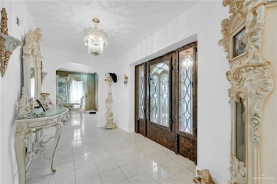 Foyer featuring arched walkways, a chandelier, light tile patterned floors, and baseboards