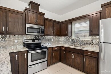 Kitchen featuring sink, dark brown cabinets, stainless steel appliances, light stone countertops, and backsplash