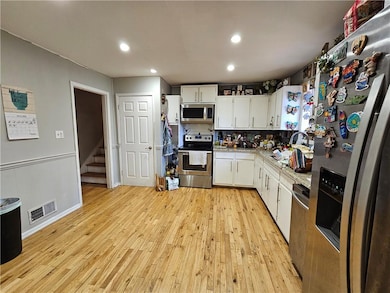 Kitchen with appliances with stainless steel finishes, light wood-style floors, light countertops, white cabinets, and backsplash
