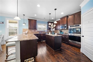 Kitchen with a peninsula, backsplash, appliances with stainless steel finishes, crown molding, and a kitchen island