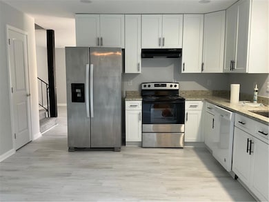 Kitchen with appliances with stainless steel finishes, light stone counters, white cabinetry, light wood-style floors, and extractor fan