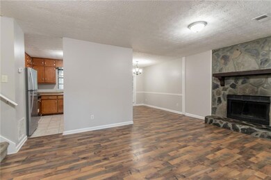 Unfurnished living room featuring wood finished floors, a textured ceiling, a fireplace, baseboards, and a chandelier
