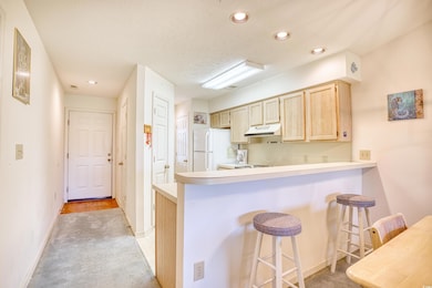 Kitchen with premium range hood, light brown cabinets, light colored carpet, a breakfast bar area, and white fridge