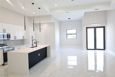 Kitchen featuring appliances with stainless steel finishes, light marble finish floors, white cabinets, a kitchen island with sink, and a raised ceiling