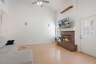 Unfurnished living room with high vaulted ceiling, light wood-type flooring, ceiling fan, and a glass covered fireplace