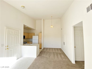 Kitchen featuring light brown cabinetry, freestanding refrigerator, decorative light fixtures, light carpet, and a peninsula