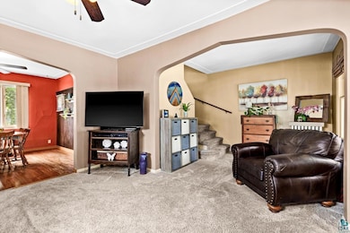 Carpeted living area featuring arched walkways, ceiling fan, and stairs