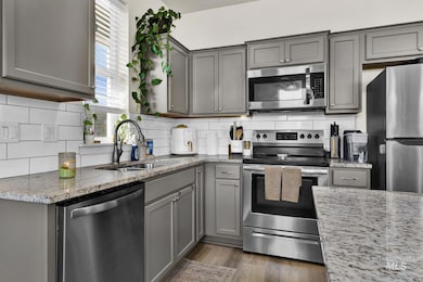 Kitchen featuring appliances with stainless steel finishes, gray cabinetry, tasteful backsplash, and light stone counters