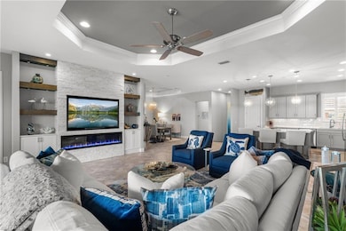 Living area featuring built in features, ornamental molding, a tray ceiling, recessed lighting, and ceiling fan