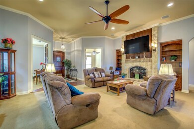 Carpeted living room featuring crown molding, a brick fireplace, ceiling fan, built in shelves, and recessed lighting