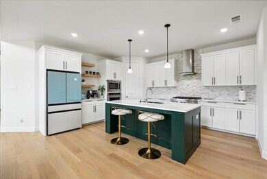 Kitchen with open shelves, stainless steel appliances, white cabinetry, wall chimney exhaust hood, and a sink