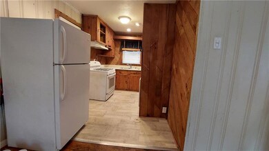 Kitchen with white appliances, brown cabinetry, wooden walls, light countertops, and under cabinet range hood