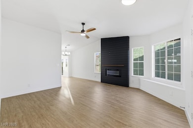 Living room with vaulted ceiling, a fireplace, light wood-style flooring, a ceiling fan, and a chandelier