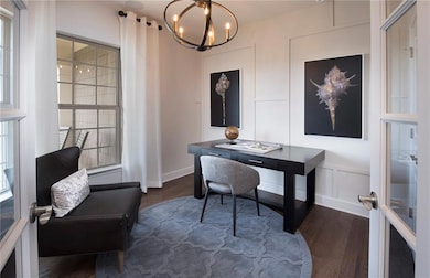 Home office with dark wood-type flooring, plenty of natural light, a chandelier, a decorative wall, and french doors