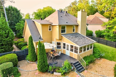 Rear view of house with a sunroom, a deck, a chimney, and a shingled roof