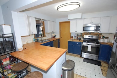 Kitchen featuring white cabinetry, blue cabinetry, a peninsula, stainless steel appliances, and tasteful backsplash