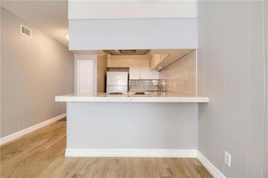Kitchen featuring tasteful backsplash, light wood-style floors, freestanding refrigerator, a peninsula, and a textured ceiling