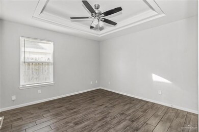 Empty room featuring a tray ceiling, dark wood-style floors, and a ceiling fan