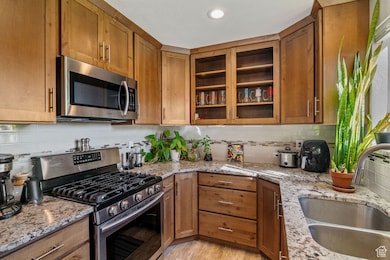 Kitchen featuring appliances with stainless steel finishes, brown cabinetry, tasteful backsplash, light stone countertops, and recessed lighting