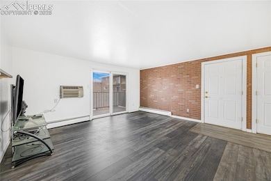 Unfurnished living room featuring dark wood-style floors, baseboard heating, brick wall, and an AC wall unit