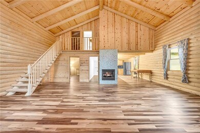 Unfurnished living room with high vaulted ceiling, wooden ceiling with exposed beams, log walls, a glass covered fireplace, and wood finished floors