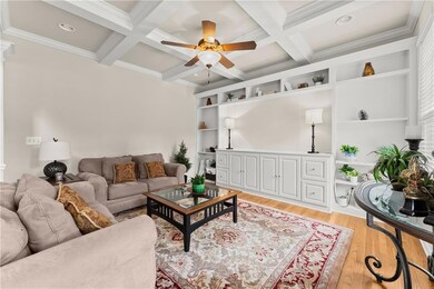 Living room featuring ceiling fan, beam ceiling, light wood-style floors, ornamental molding, and coffered ceiling