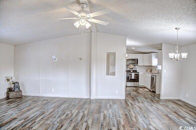 Unfurnished living room featuring a textured ceiling, wood finished floors, lofted ceiling, a chandelier, and ceiling fan