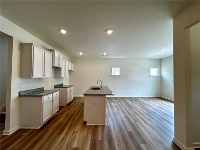Kitchen featuring dark wood finished floors, dark stone countertops, an island with sink, recessed lighting, and white cabinets