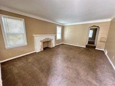 Unfurnished living room with dark colored carpet, arched walkways, a stone fireplace, and ornamental molding
