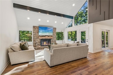 Living room with beam ceiling, high vaulted ceiling, wooden ceiling, wood-type flooring, and a stone fireplace