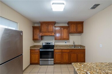 Kitchen featuring appliances with stainless steel finishes, light stone countertops, brown cabinetry, and a textured ceiling