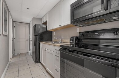 Kitchen featuring black appliances, white cabinetry, light tile patterned flooring, and light stone countertops