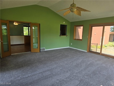 Spare room featuring ceiling fan, lofted ceiling, dark carpet, and french doors