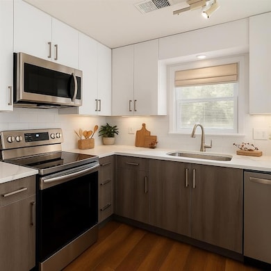 Kitchen featuring appliances with stainless steel finishes, white cabinetry, dark wood-type flooring, and tasteful backsplash