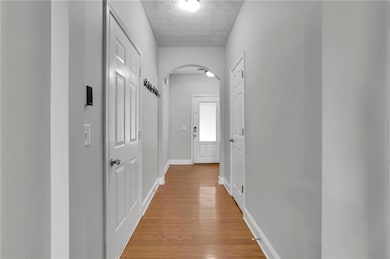 Hall featuring arched walkways, light wood finished floors, and a textured ceiling