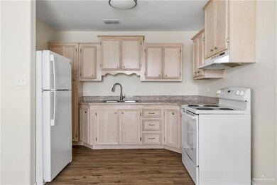 Kitchen with a sink, visible vents, white appliances, light brown cabinets, and under cabinet range hood
