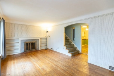 Living room featuring wallpapered walls, stairway, light wood floors, a fireplace, and arched walkways