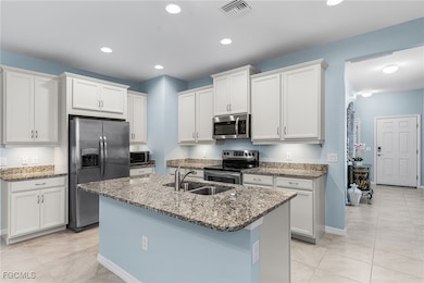 Kitchen with appliances with stainless steel finishes, light stone countertops, white cabinets, light tile patterned floors, and an island with sink