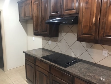 Kitchen featuring ventilation hood, stovetop, decorative backsplash, and dark stone counters