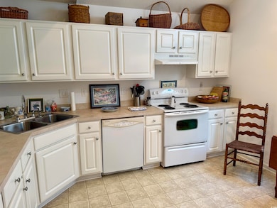 Kitchen featuring white appliances, under cabinet range hood, white cabinetry, and light countertops
