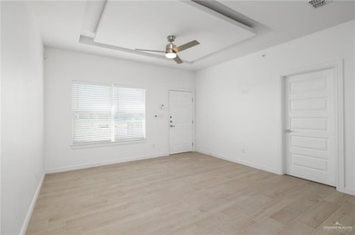 Empty room featuring light wood-type flooring, a tray ceiling, and ceiling fan