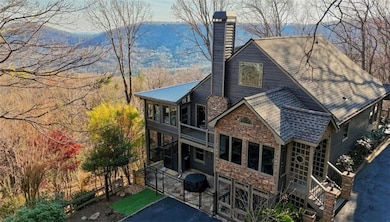 Rear view of house featuring stone siding, a gate, a sunroom, a chimney, and stairs