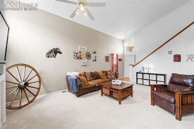 Carpeted living room with ceiling fan and high vau