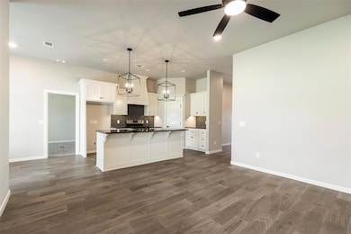 Kitchen featuring backsplash, a kitchen bar, white cabinetry, hanging light fixtures, and a kitchen island with sink