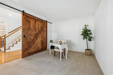 Office space featuring a barn door, ornamental molding, and carpet flooring