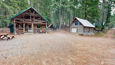 Front view of the cabin with covered porch, detached log garage, and wooded setting offering privacy and charm.