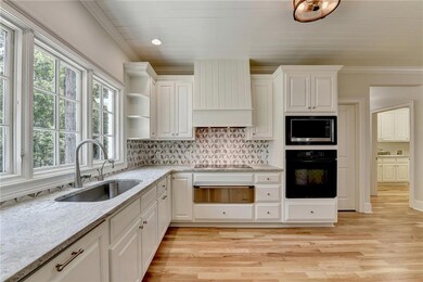 Kitchen featuring black appliances, light wood finished floors, custom range hood, ornamental molding, and open shelves