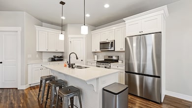 Kitchen with stainless steel appliances, light stone counters, an island with sink, a breakfast bar, and dark wood-style floors