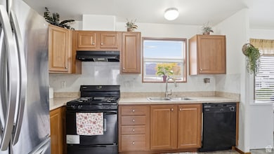 Kitchen with black appliances, tasteful backsplash, light countertops, under cabinet range hood, and brown cabinets