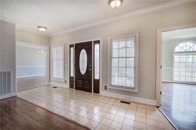 Foyer entrance with light wood-type flooring, ornamental molding, visible vents, and a chandelier